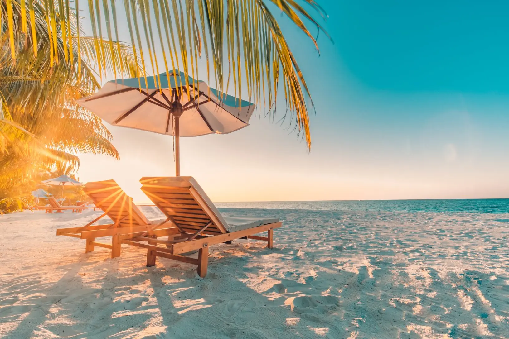 Two loungers under an umbrella on a quiet beach at sunset